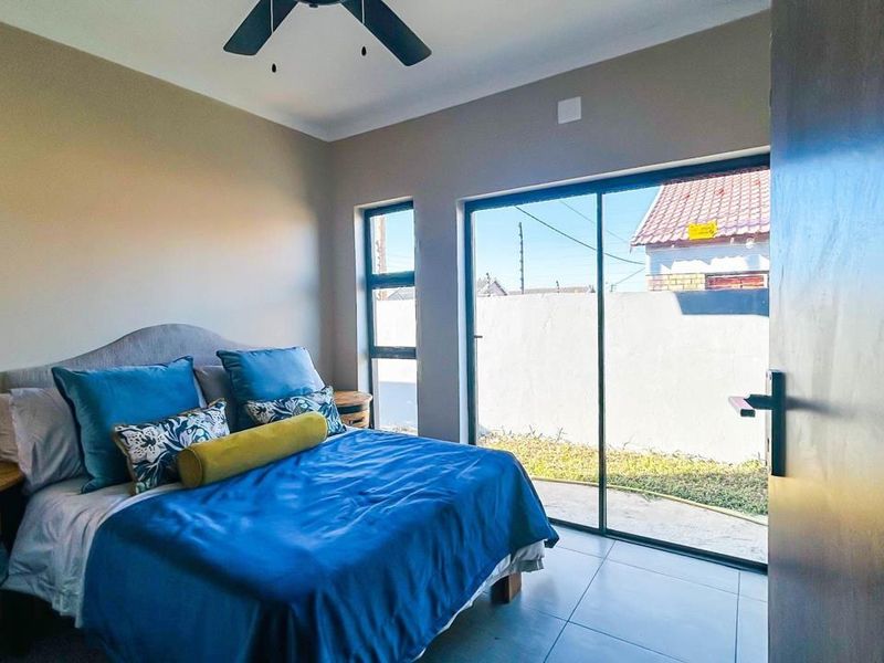 A bright bedroom featuring tiled flooring, a ceiling fan, and large sliding glass doors that provide direct access to the outdoor area.