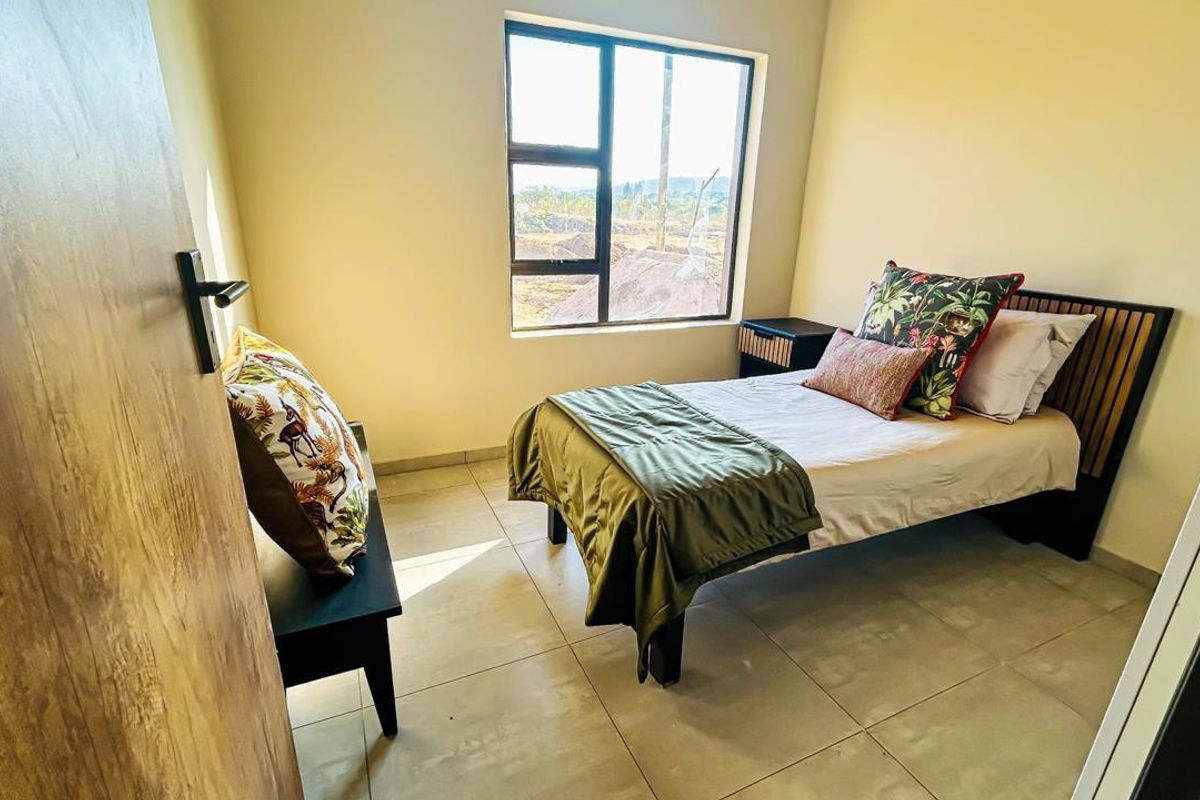 A well-lit bedroom featuring neutral tiled flooring and a large aluminium-framed window, providing a clean and functional living space.