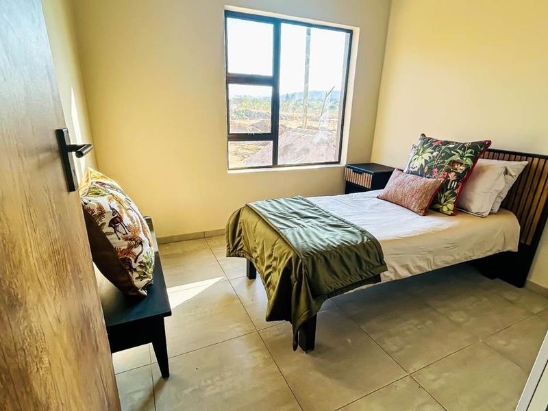 A well-lit bedroom featuring neutral tiled flooring and a large aluminium-framed window, providing a clean and functional living space.