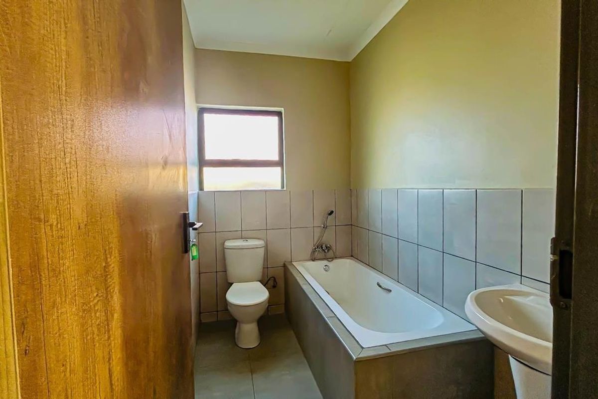 A functional bathroom featuring a built-in bathtub, toilet, and pedestal basin with neutral wall tones and tiled splashbacks.