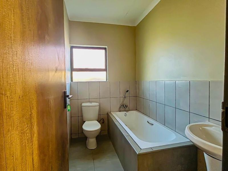 A functional bathroom featuring a built-in bathtub, toilet, and pedestal basin with neutral wall tones and tiled splashbacks.