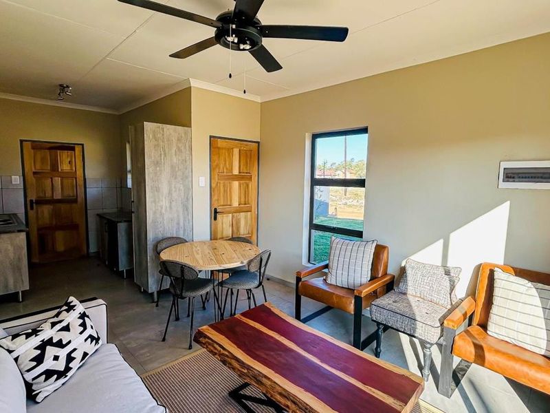 An open-plan living and kitchen area featuring tiled flooring, a ceiling fan, and functional built-in cabinetry with a sink.