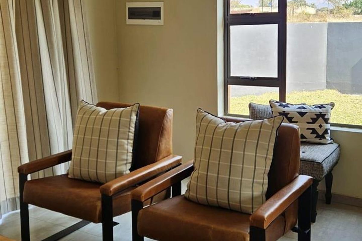 A well-lit living area featuring tiled flooring, a large aluminium window with a roman blind, and neutral wall finishes.