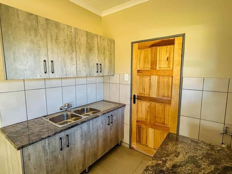 A functional scullery area featuring built-in cabinetry, a double stainless steel sink, and tiled splashbacks, providing additional workspace and utility.