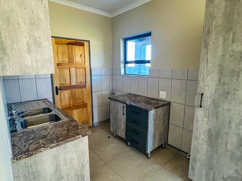 A functional scullery area featuring built-in cabinetry, laminate countertops, a double stainless steel sink, and tiled finishes throughout.