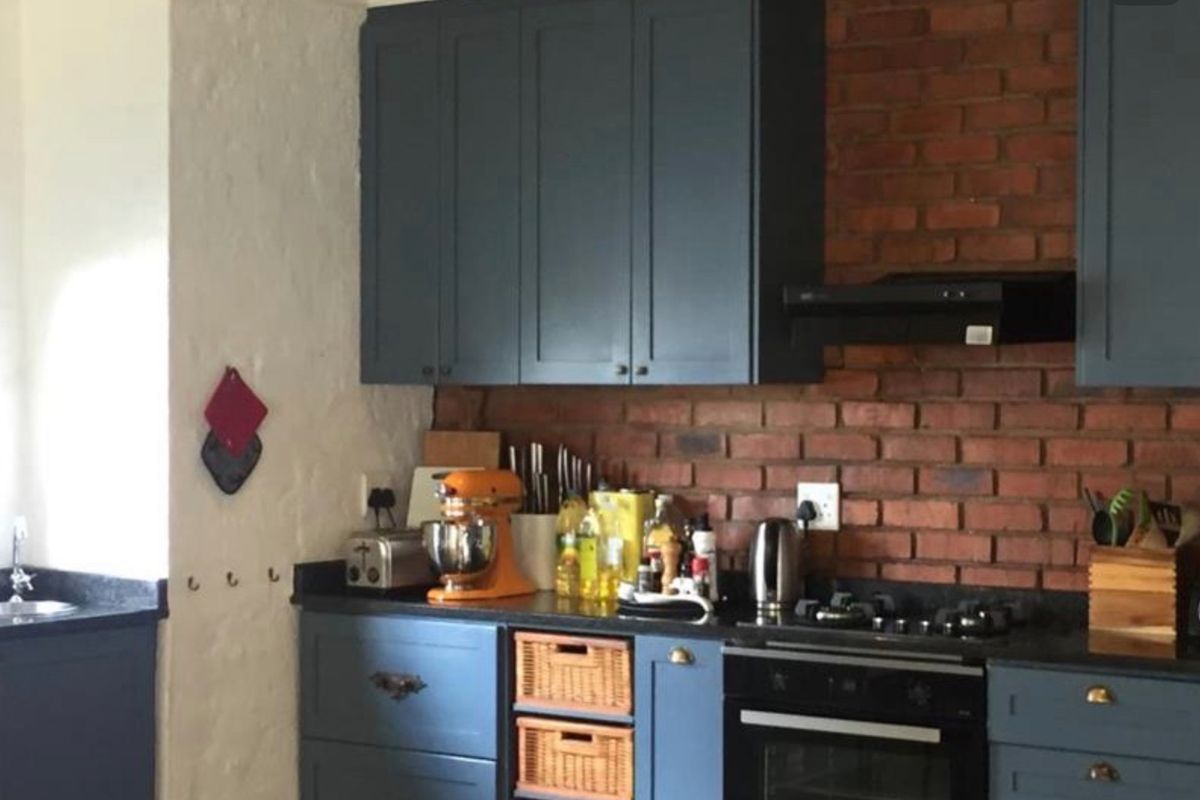 A well-maintained kitchen featuring dark blue cabinetry, a striking exposed brick backsplash, built-in oven, gas hob, and stone countertops.