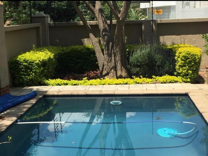 A private swimming pool area featuring a paved surround, established garden landscaping, and secure perimeter walling with electric fencing.