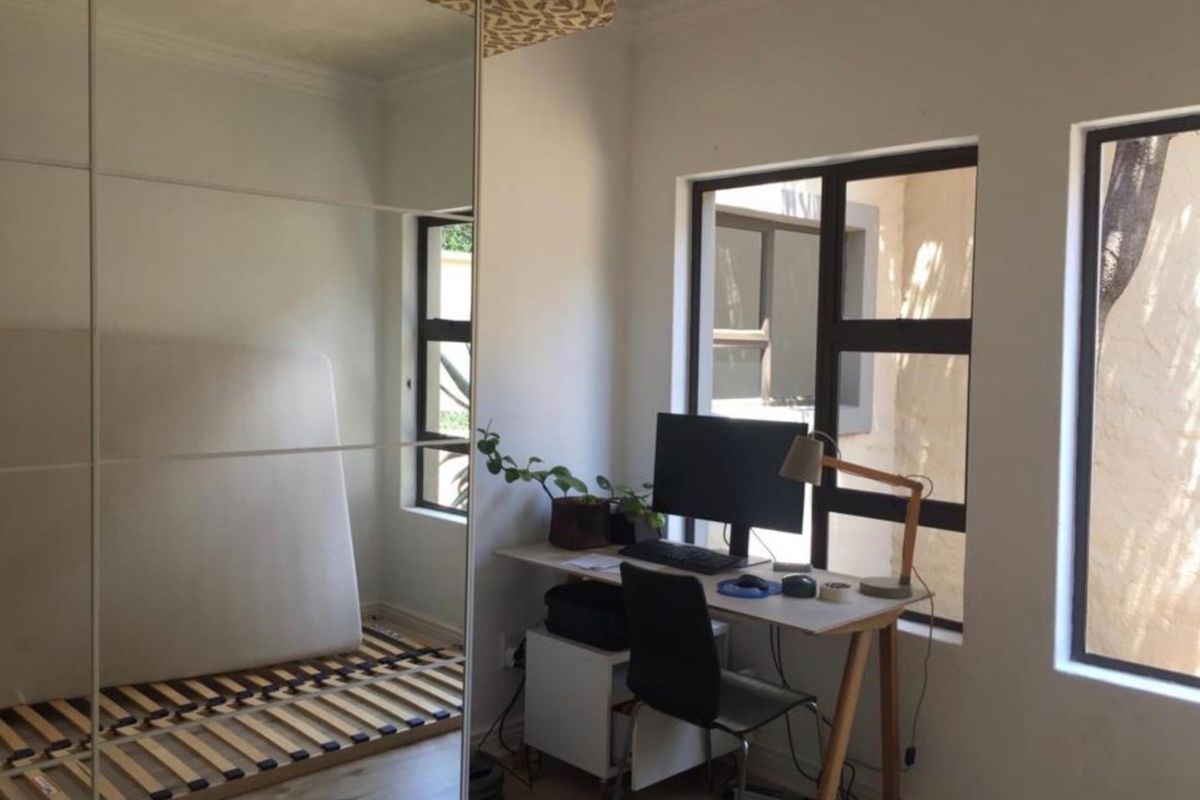 A bedroom featuring a large built-in mirrored wardrobe, laminate flooring, and aluminium-framed windows providing natural light.