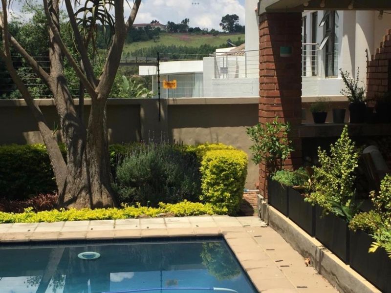 Outdoor pool area featuring a paved surround, brick structural pillar, and established garden landscaping with boundary wall and electric security fencing.