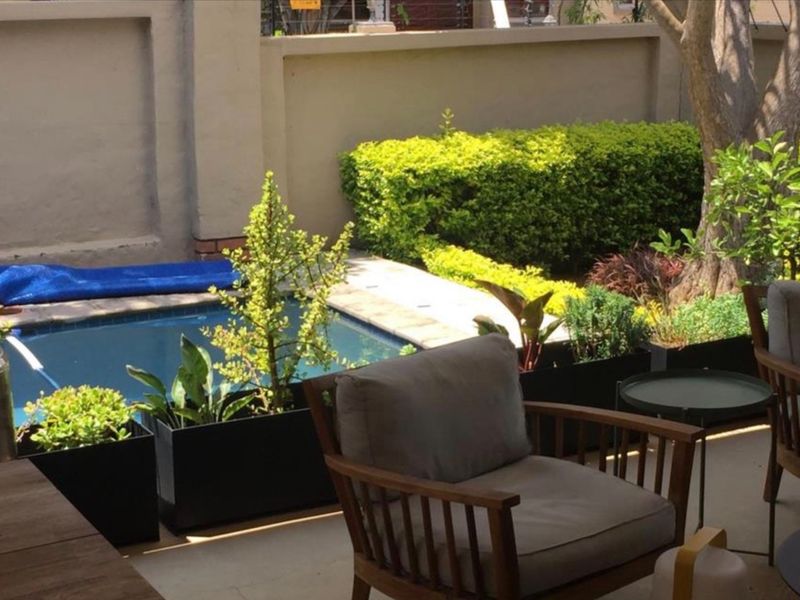 A private outdoor pool area featuring a paved patio, boundary wall, and established garden landscaping.