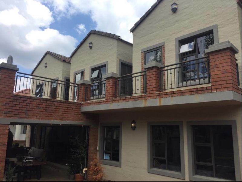 Rear view of a multi-story home featuring a brick and plaster facade, upper-level balcony with wrought iron railings, and a covered ground-floor patio area.