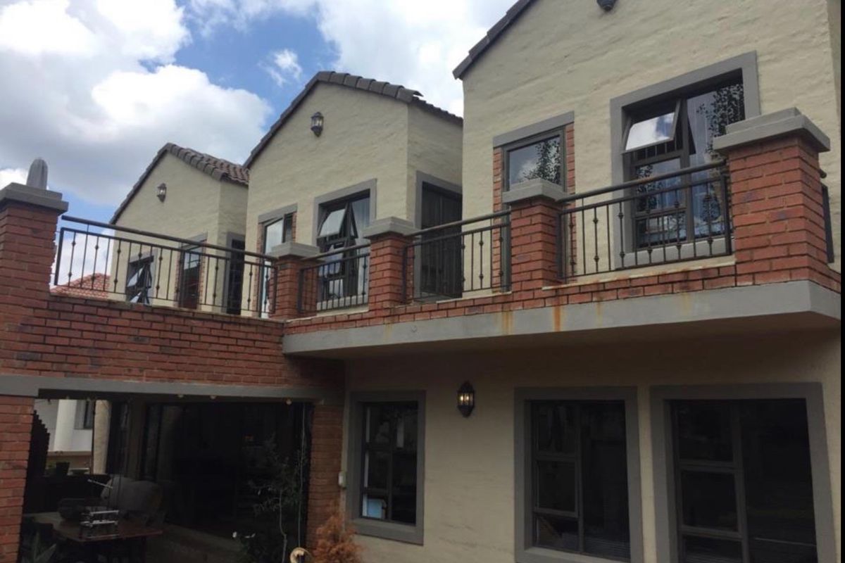 Rear view of a multi-story home featuring a brick and plaster facade, upper-level balcony with wrought iron railings, and a covered ground-floor patio area.