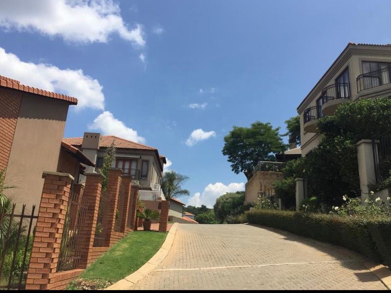 A view of a residential street featuring paved driveways, brick boundary walls, and multi-story homes with tiled roofs and balconies.