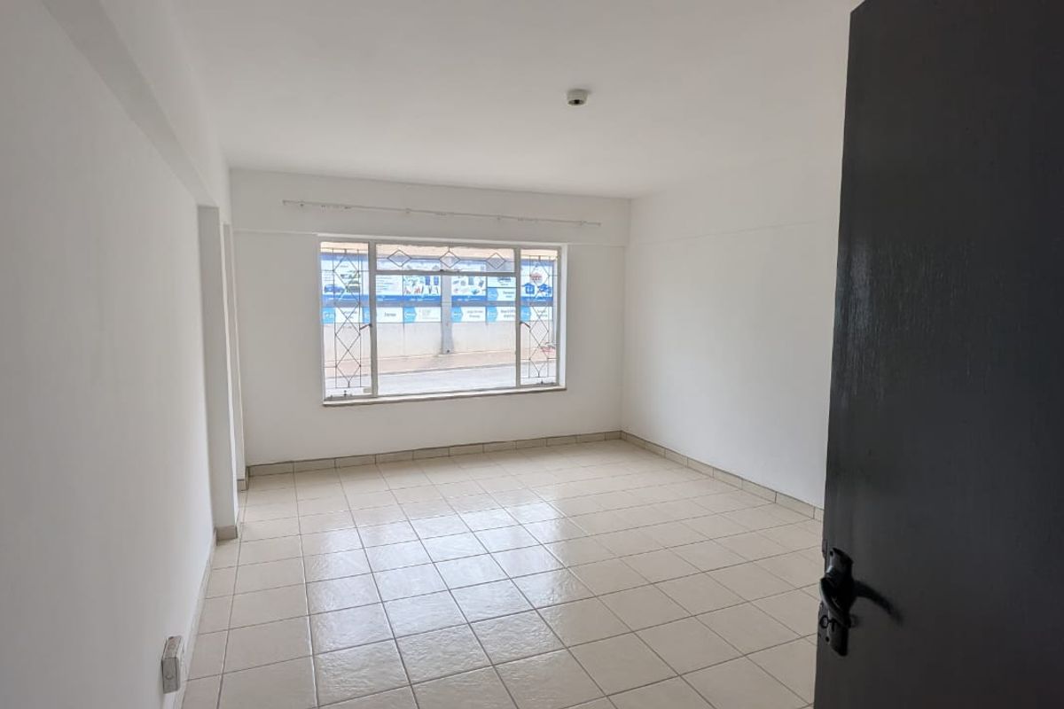 A bright, empty living area featuring neutral tiled flooring and a large window with security bars, offering a blank canvas for personalization.