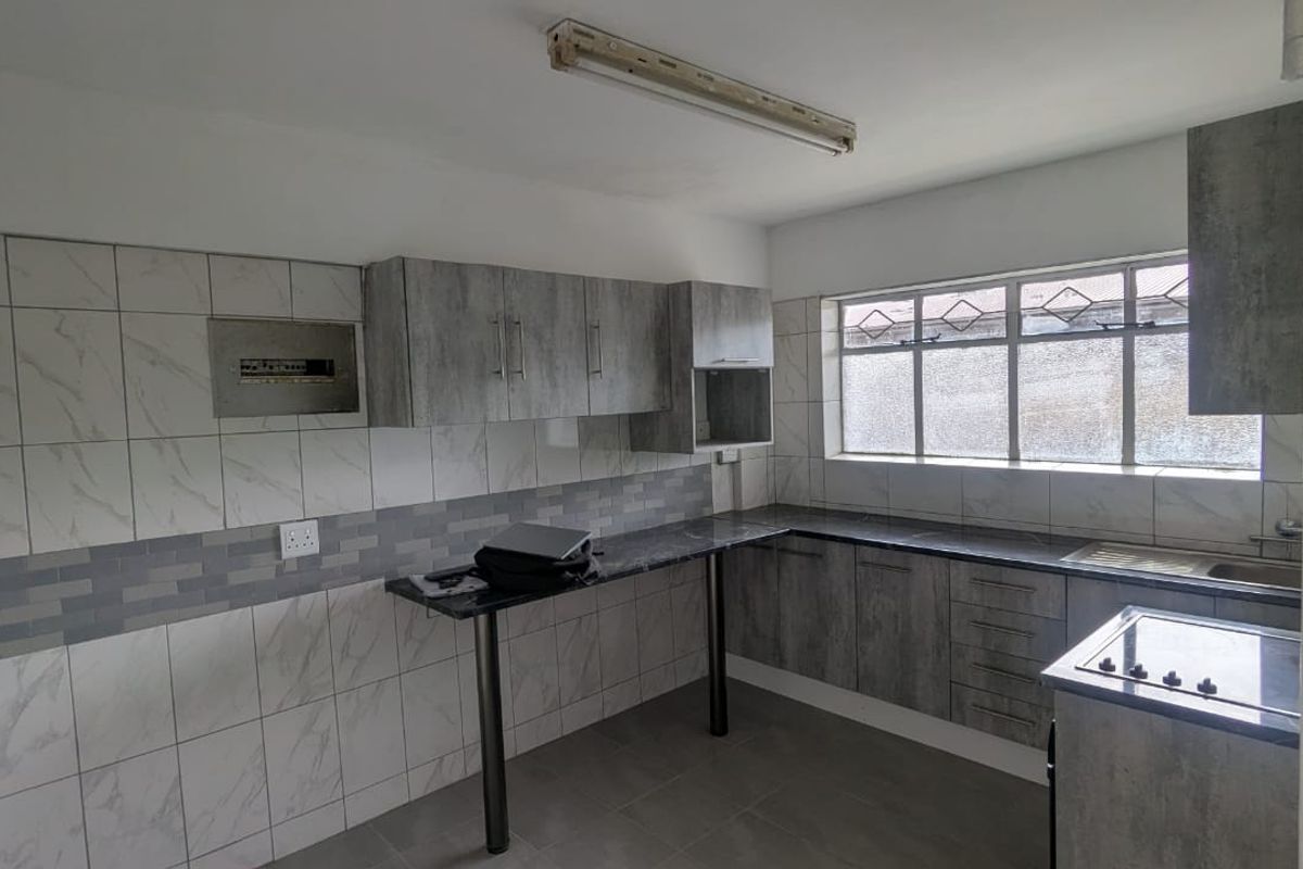A functional kitchen featuring grey wood-look cabinetry, dark countertops, tiled walls, and a built-in hob, offering a clean and practical workspace.
