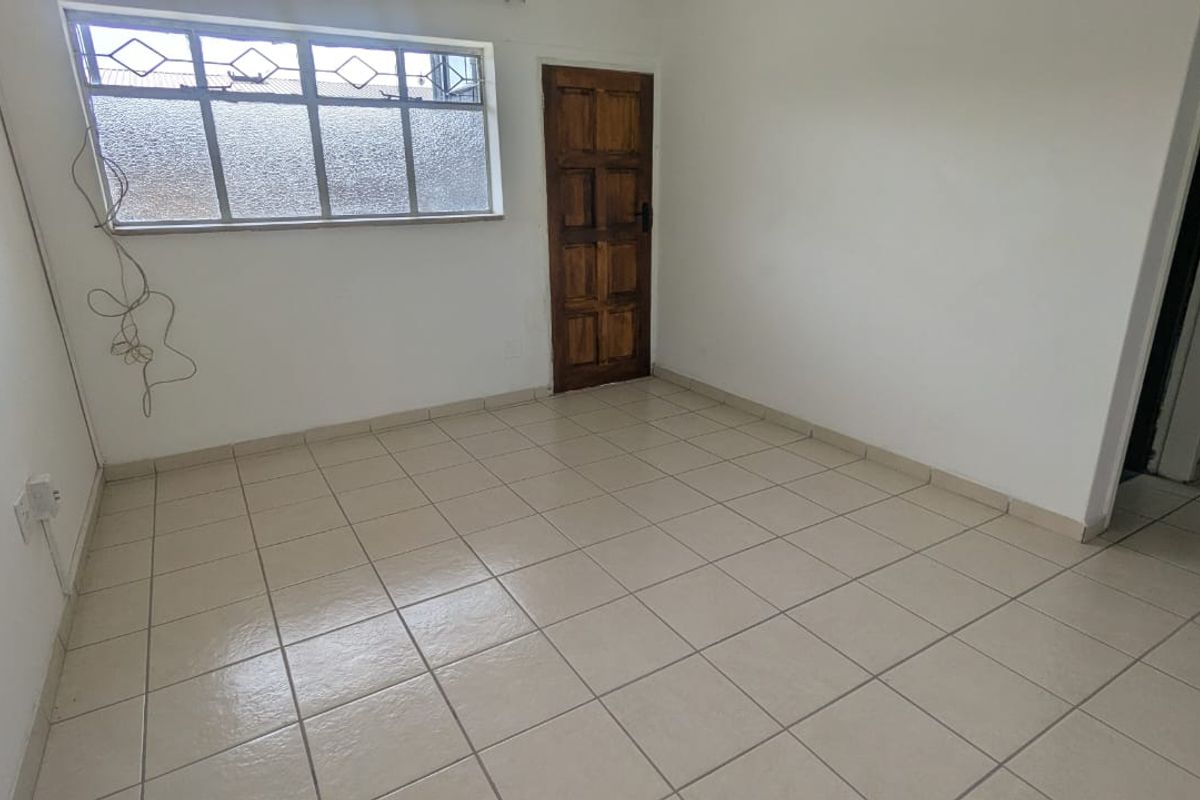 An empty bedroom featuring neutral tiled flooring, a timber door, and an aluminium window frame, providing a blank canvas for interior design.