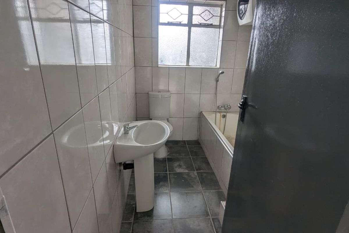 A functional bathroom featuring a pedestal basin, toilet, and bathtub with tiled walls and flooring, requiring cosmetic updates to improve its overall condition.