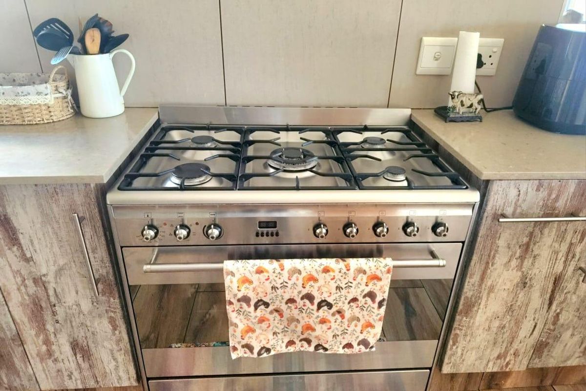 A close-up view of a stainless steel gas stove and oven integrated into stone countertops with a tiled backsplash and textured cabinetry.