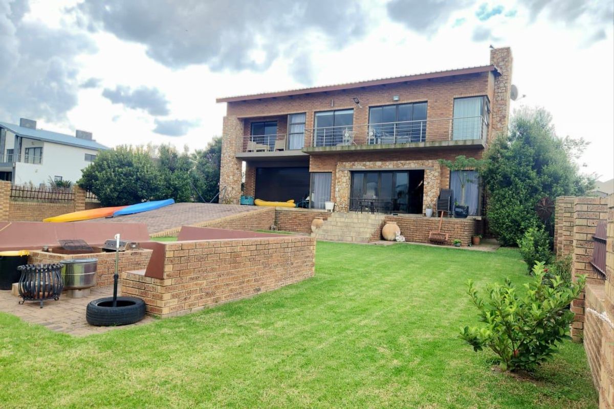 Rear view of a two-story brick house featuring a stone-clad facade, upper balcony with metal railings, paved patio, and a built-in brick fire pit.
