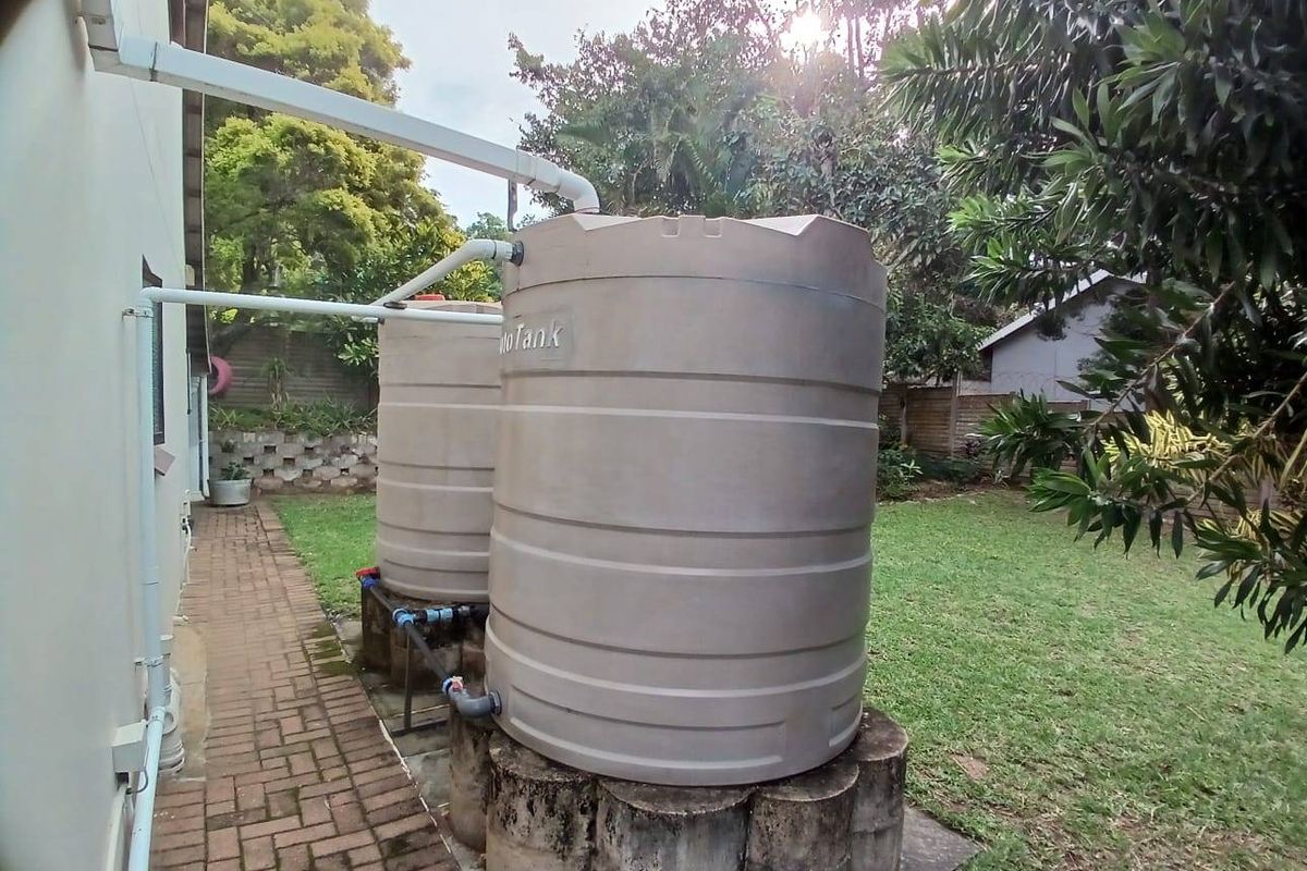 Rear garden area featuring two large water storage tanks connected to the building's guttering system, set alongside a paved walkway.