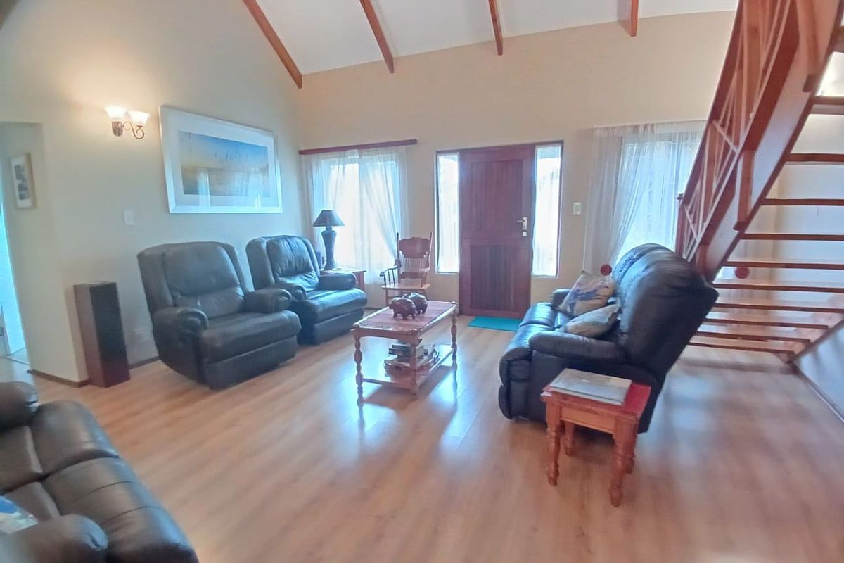 Spacious living room featuring vaulted ceilings with exposed timber rafters, laminate flooring, and a prominent timber staircase leading to the upper level.
