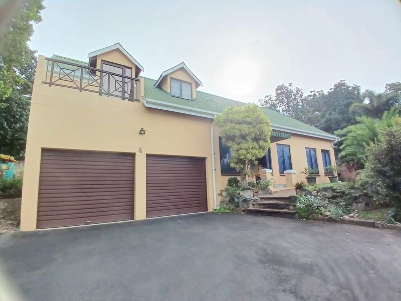 Front elevation of a townhouse featuring a double garage, asphalt driveway, and an upper-level balcony with metal railings.
