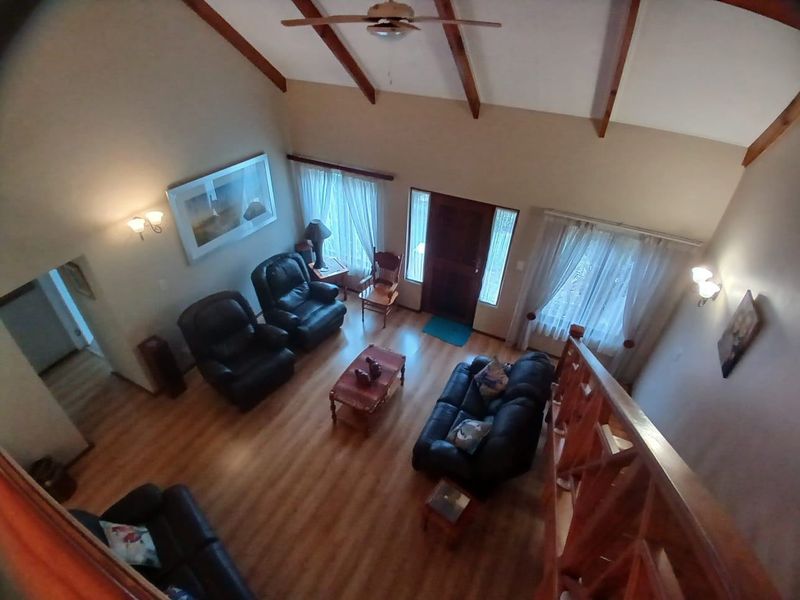 Spacious living room featuring a high vaulted ceiling with exposed timber beams, laminate flooring, and a timber staircase railing.