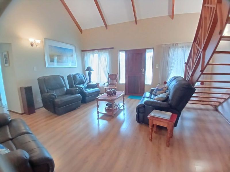 Spacious living room featuring vaulted ceilings with exposed timber rafters, laminate flooring, and a prominent timber staircase leading to the upper level.