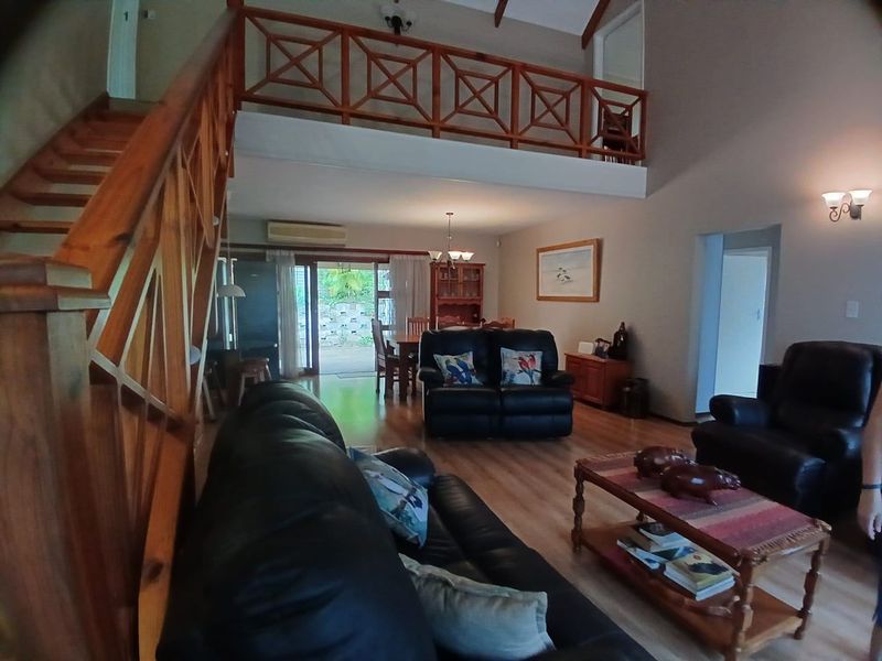 Spacious open-plan living and dining area featuring a timber staircase, mezzanine level, vaulted ceilings, and direct access to the outdoor patio.
