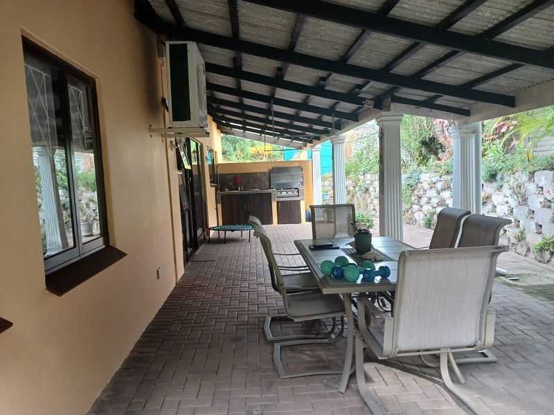 A spacious covered patio featuring paved flooring, a built-in braai area with cabinetry, and direct access to the garden and retaining wall.