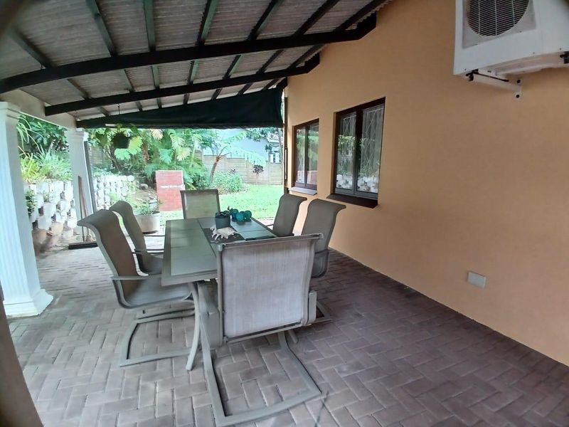 A covered outdoor patio area featuring paved flooring and an installed air conditioning unit, providing a functional space for outdoor dining and relaxation.