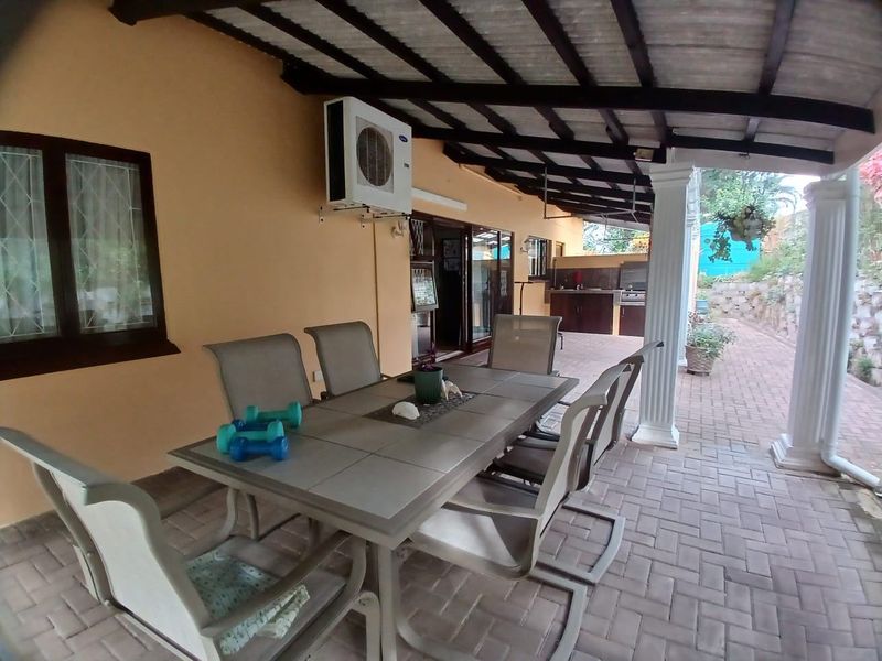 A covered outdoor patio featuring brick paving, decorative columns, and a built-in braai area, providing a functional space for outdoor dining and relaxation.