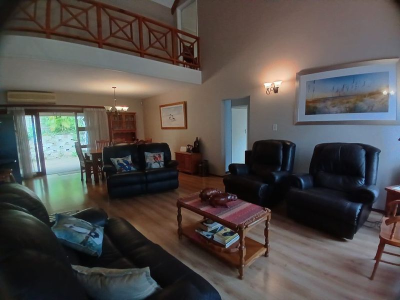 Spacious open-plan living area featuring high vaulted ceilings, a mezzanine level with wooden balustrade, laminate flooring, and sliding doors leading to the patio.