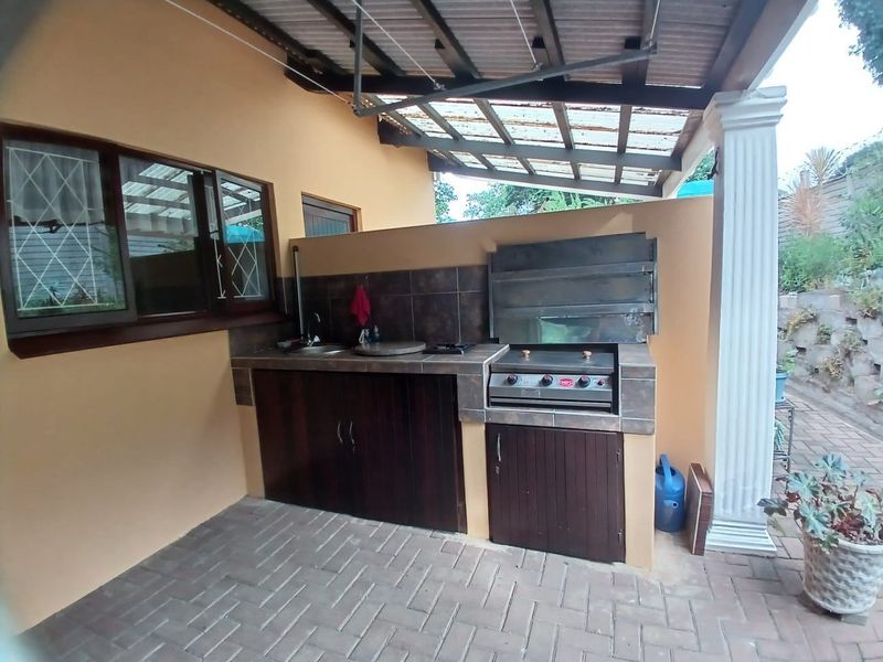 Covered outdoor patio featuring a built-in braai, tiled prep area with sink, and under-counter storage, ideal for outdoor entertaining.