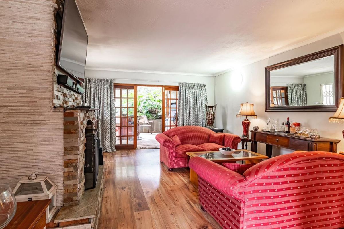 Spacious living room featuring a stone-clad fireplace, wood-look flooring, and French doors providing direct access to the outdoor patio area.