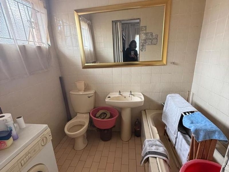 A dated bathroom featuring a pedestal basin, toilet, and bathtub with tiled walls and flooring. The space includes a laundry appliance connection.