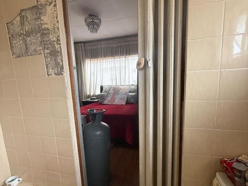 A bathroom interior showing a built-in bathtub and tiled walls with visible damage, featuring a folding door leading into an adjacent bedroom.