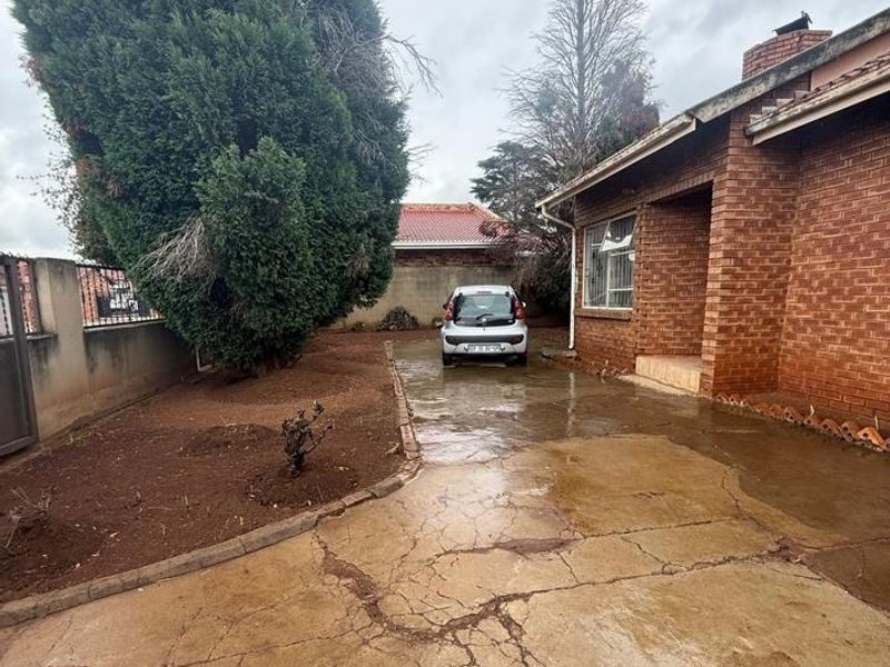 Front exterior view of a brick house featuring a driveway with significant cracking and a boundary wall.