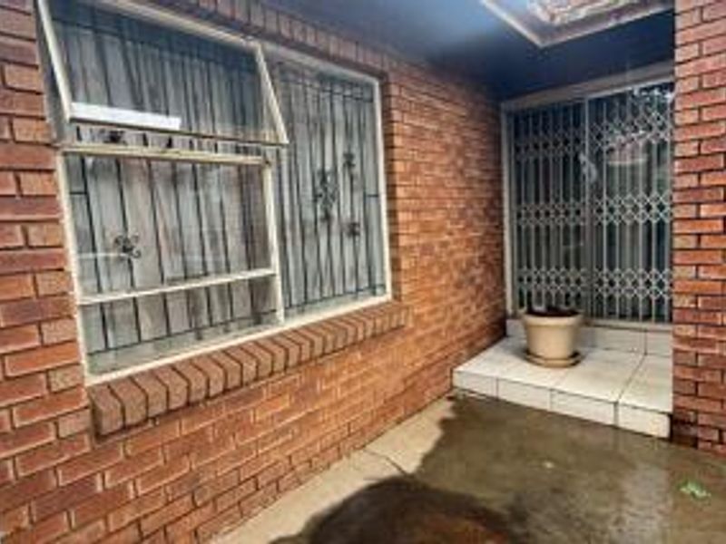 A covered brick patio area featuring tiled flooring and security bars on the windows and sliding door entrance.