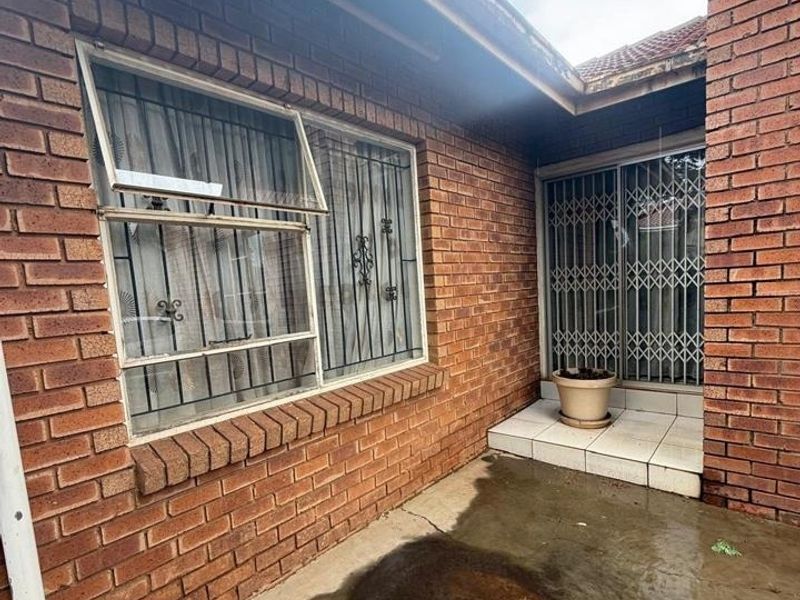 Rear exterior view of the house featuring face brick walls, security bars on windows, and a concrete patio area showing signs of wear.