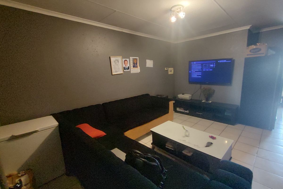 A living room area featuring tiled flooring and a wall-mounted television, requiring cosmetic updates to the wall finishes.