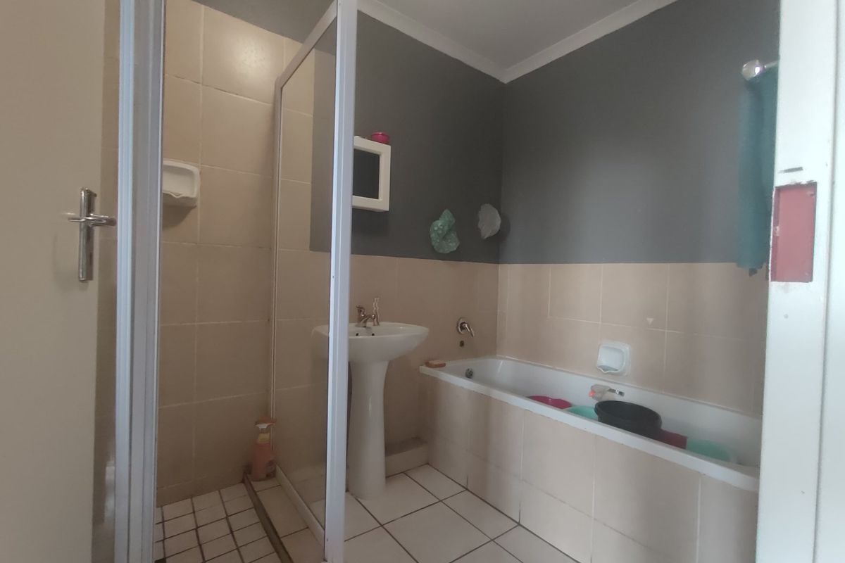 A functional bathroom featuring a pedestal basin, a built-in bathtub, and a separate shower enclosure with tiled finishes.