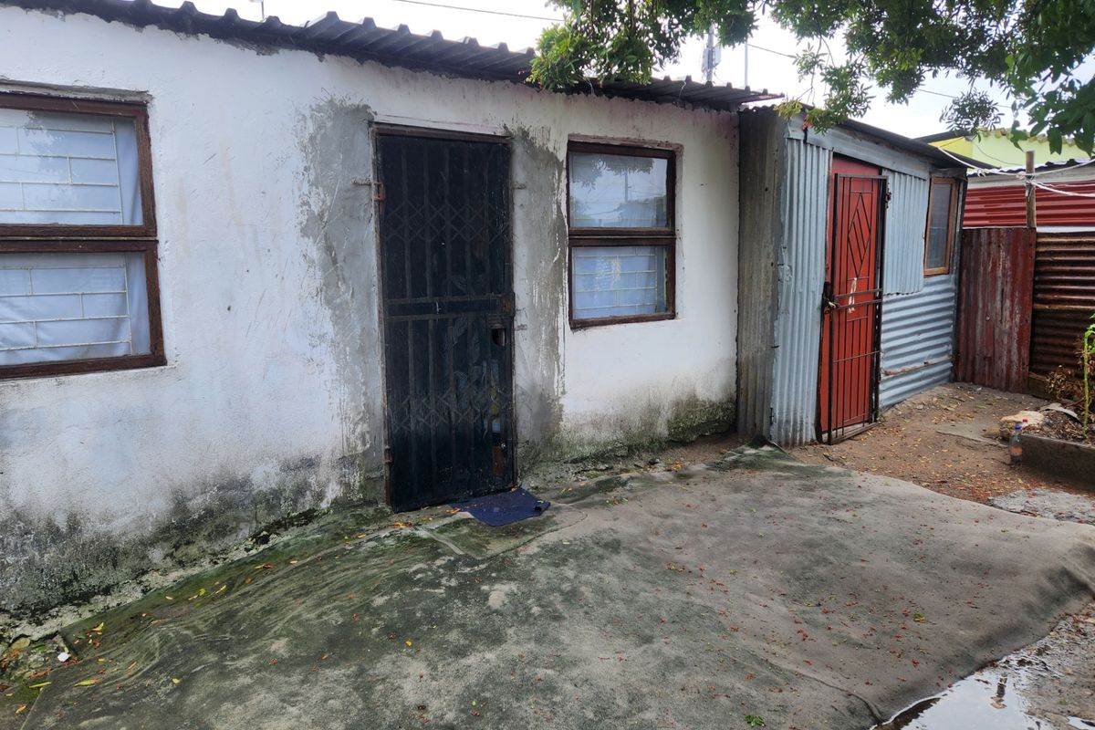 Rear exterior view of a modest dwelling featuring a concrete patio, security gates, and weathered wall finishes requiring maintenance.