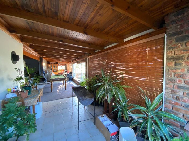 A covered patio area featuring exposed timber beam ceilings, tiled flooring, and an exposed brick wall, providing a versatile outdoor entertainment space.