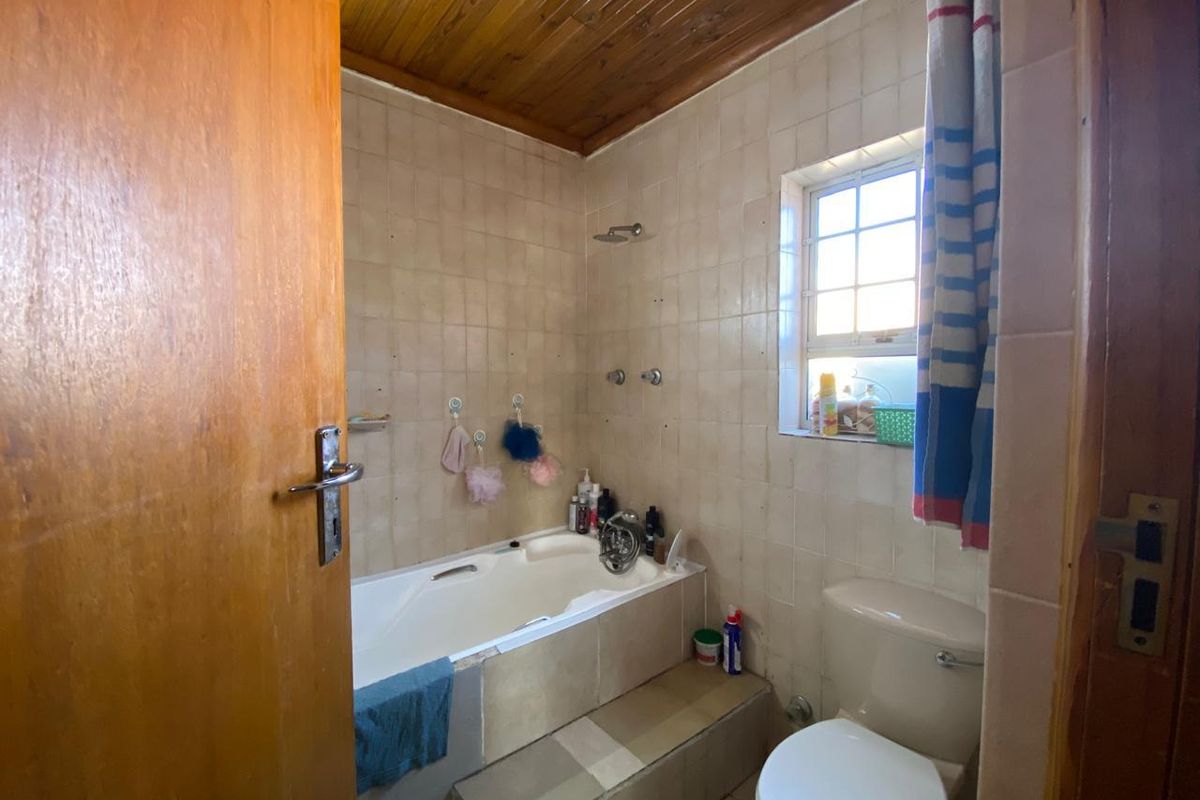 A compact bathroom featuring a built-in bathtub with shower head, toilet, tiled walls, and a timber-paneled ceiling.