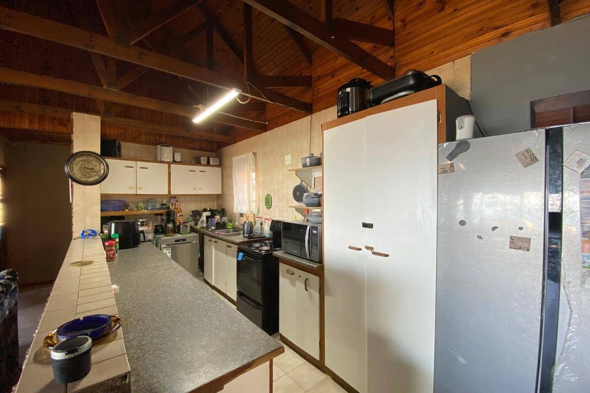 A functional kitchen featuring a breakfast bar, exposed timber ceiling beams, and ample built-in cabinetry, offering potential for a modern renovation.