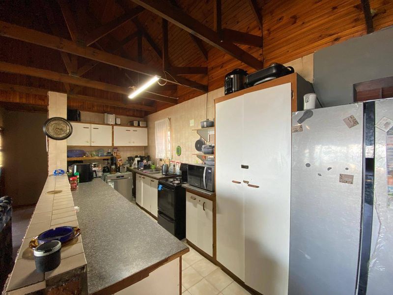 A functional kitchen featuring a breakfast bar, exposed timber ceiling beams, and ample built-in cabinetry, offering potential for a modern renovation.