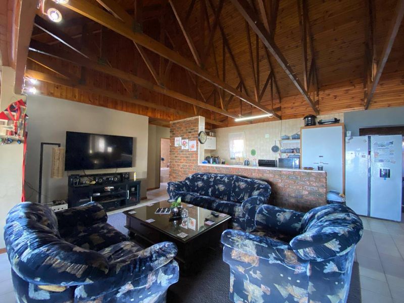 Open plan living area featuring high exposed timber ceilings, brick feature wall, and a functional kitchen layout with a breakfast bar.