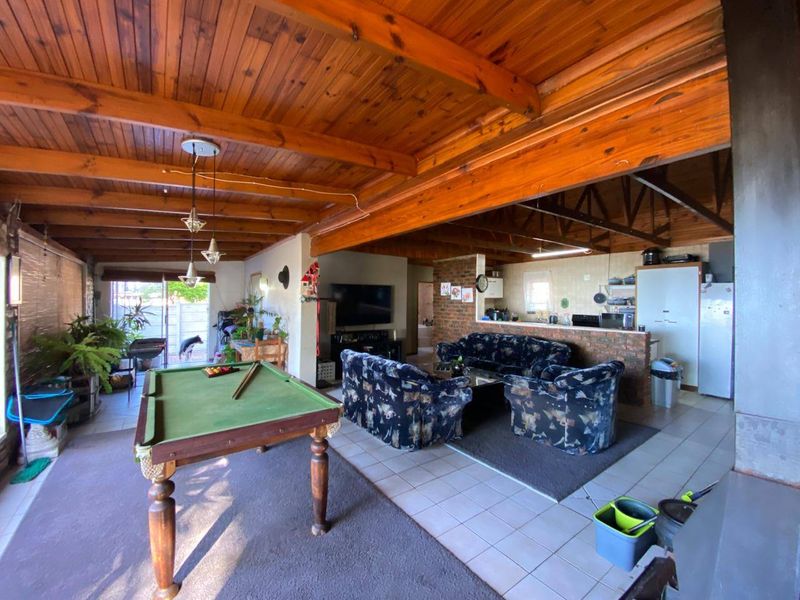 Spacious open-plan living area featuring exposed timber beam ceilings, a brick breakfast bar, and tiled flooring, creating a versatile and functional family space.