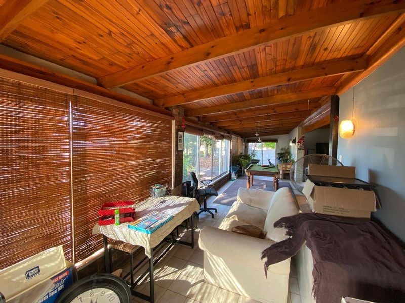 Spacious covered patio featuring an exposed timber beam ceiling, tiled flooring, and large sliding glass doors providing access to the garden area.